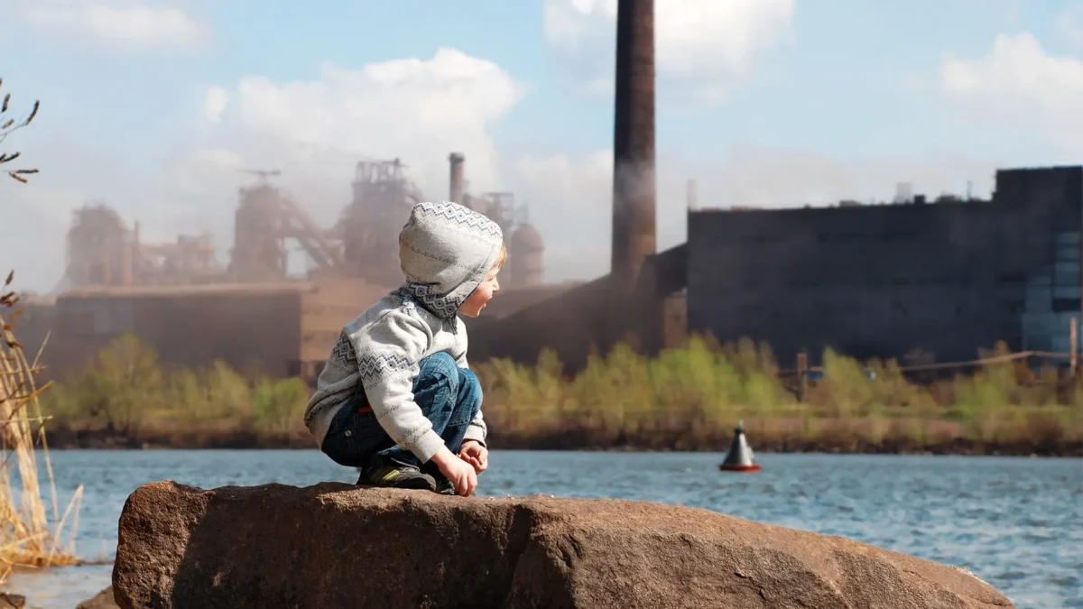 Playing a little boy on the river coast in front of a metallurgical plant