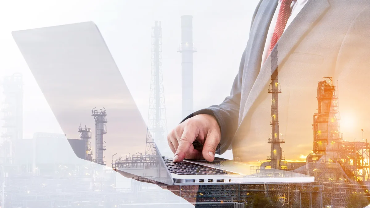 Businessman using a laptop with a blurred refinery plant background